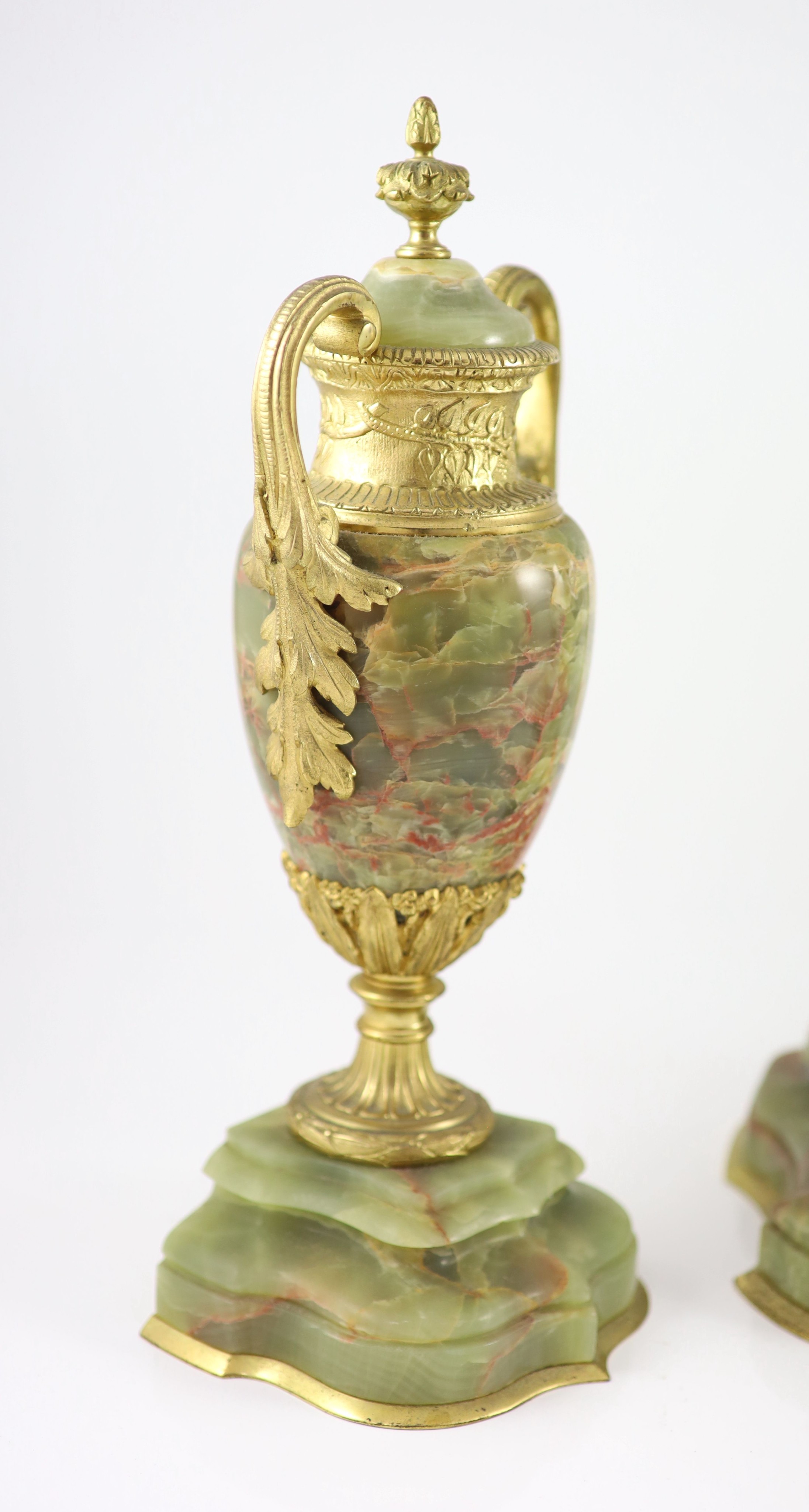 A green onyx and gilt metal clock garniture, comprising a four-glass regulator with enamelled dial in serpentine case and a pair of pedestal urns and covers Clock H 35cm. W 27cm. Urns H 36cm.